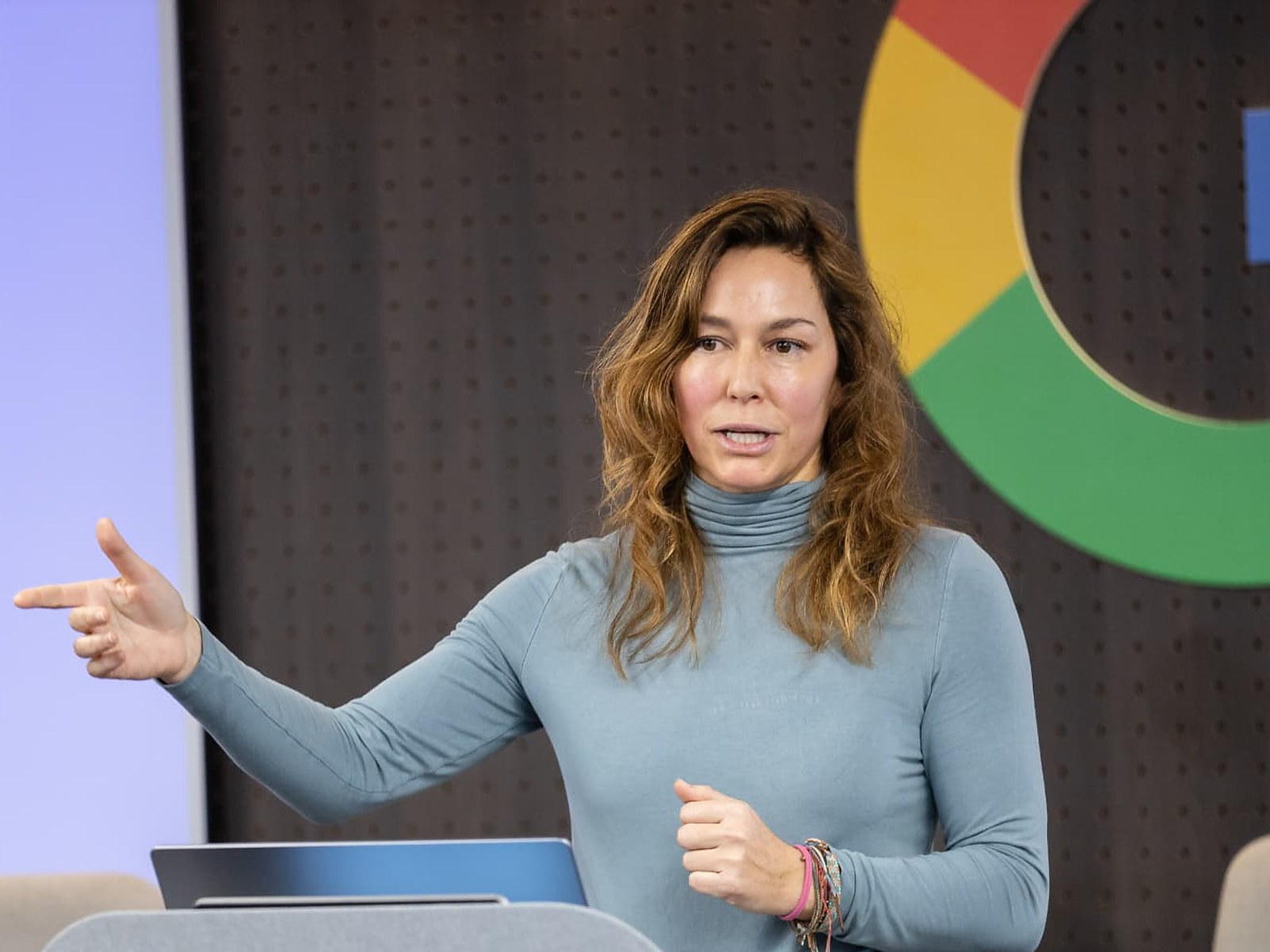 Aline presenting to an audience in front of a Google logo wall